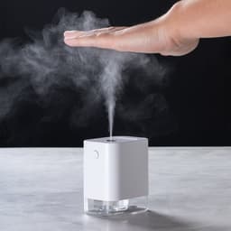 A white hand sanitiser dispenser releases a fine mist, with a hand positioned above it.