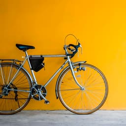 A silver bicycle with a black bike bag attached, set against a vibrant yellow wall.
