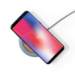 A wireless charger with a grey base, featuring a smartphone displaying a battery charging icon on top.