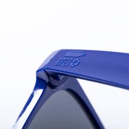 A pair of blue sunglasses with a logo detail on the arm, featuring dark lenses and a sleek design.