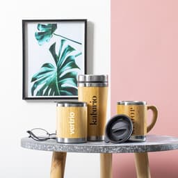 A set of bamboo insulated cups in various sizes with stainless steel details, displayed on a table beside a plant print.