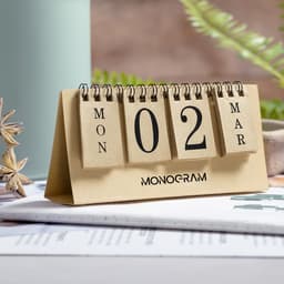 A desk calendar with a tan base, featuring black numbered and day tabs, and a logo at the bottom.