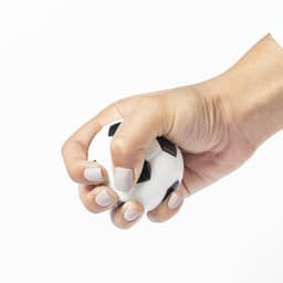 A white stress ball shaped like a soccer ball, held tightly in a hand with light-coloured nails.