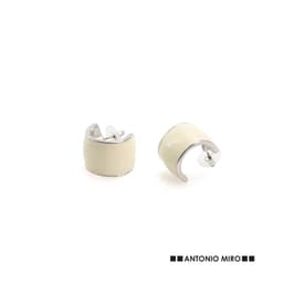 A pair of cream-coloured cuff earrings with silver accents, featuring a logo.
