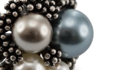 A close-up of a Pleus Adjustable Ring featuring various pearls in silver and blue hues, set within a textured black design.