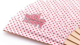 A hand fan featuring a polka dot design in pink and white, with a logo on the surface.