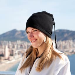 A black beanie hat with a drawstring, worn by a woman against a scenic city and mountain backdrop.
