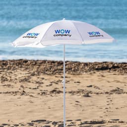 A white beach umbrella with a logo, set against a sandy beach and ocean backdrop.