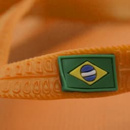 A pair of orange thongs featuring a green and blue logo resembling the Brazilian flag.