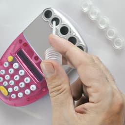 A pink calculator with a hand holding a clear tube above it, with several circular compartments visible.