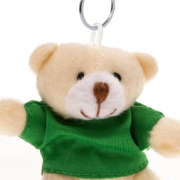 A keyring teddy bear with a light brown body and a green shirt, featuring a smiling face and raised arms.
