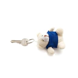 A keyring featuring a small white teddy bear wearing a blue outfit, attached to a key.