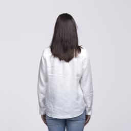 A white linen button-up shirt viewed from the back, worn by a woman with long hair, paired with blue jeans.