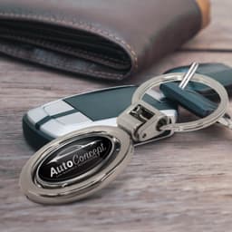 A silver spinning metal key ring displayed alongside a car key and a brown wallet. The key ring has a logo.