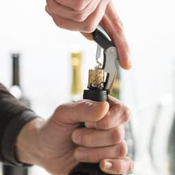 A drink bottle opener, specifically a Classic Wine Waiters Knife, is being used to remove a cork from a wine bottle.
