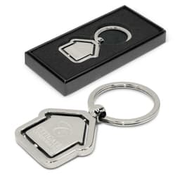 A metal key ring shaped like a house, featuring an engraved logo, presented in a sleek black gift box.
