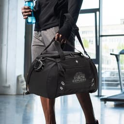 A black sports bag with a shoulder strap, being held by a person, featuring a logo and a drink bottle attached.