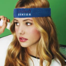 A blue head sweat band worn by a woman with long hair, set against a green background. The band features a logo.