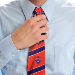 A person adjusting a red tie featuring blue patterns, worn over a light blue shirt. The tie has a logo.