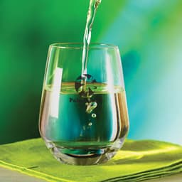 A stemless glass filled with liquid, featuring a reflective surface and a colorful background.
