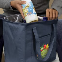 A drink bottle is being placed into a navy cooler bag with an interior lining, featuring a logo.