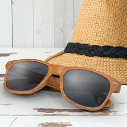 A pair of brown wooden sunglasses with dark lenses, resting on a straw hat with a black band.