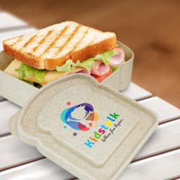 A sandwich box in a beige colour, featuring a logo and containing a sandwich with layers of ham, cheese, and lettuce.