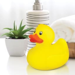 A bright yellow rubber duck next to a striped drink bottle, a small plant, and neatly stacked towels.