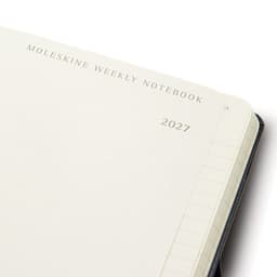 A Moleskine 2027 weekly planner in navy blue with blank pages and a branding logo on the cover.