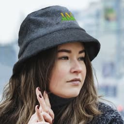 A grey terry towelling bucket hat with a logo, worn by a woman with long hair in an outdoor setting.