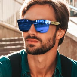 Bamboo sunglasses with blue mirror lenses worn by a man, set against a blurred outdoor background.