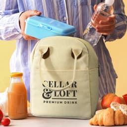 A yellow lunch bag with a logo, surrounded by a drink bottle, blue lunch box, juice, and apples.