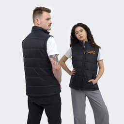 A black puffer vest featuring a logo, worn by models in a minimalist setting.