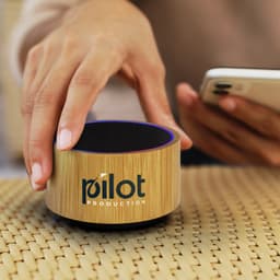 A bamboo Bluetooth speaker with a circular design and a textured surface, featuring a logo on the front.