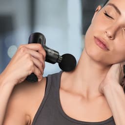 A black handheld massager is being used on a woman's neck, with a lightly blurred background.
