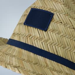 A straw fedora hat featuring a navy band and a square patch. The design showcases woven straw patterns.