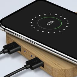 A bamboo wireless charging hub with a smartphone displaying charging status. The hub has two connected cables.