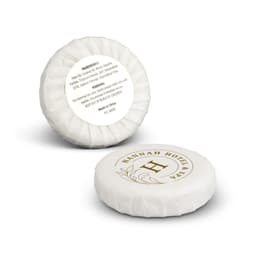 A round, white soap bar with a gold and white branded label, featuring a decorative wrapping.