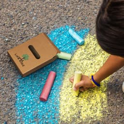 A set of jumbo sidewalk chalk pieces in various colours, with a cardboard box featuring a logo on the ground.