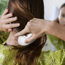 A hair detangler in use, featuring a curved white design, against a backdrop of a person with long, brown hair.