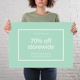 A person holds a large green sign with a white border, featuring a promotional message about storewide discounts.