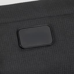A close-up of a textured black sling bag featuring a rectangular logo patch.