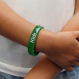 A green silicone wristband worn on a child's wrist, featuring a logo and text design.