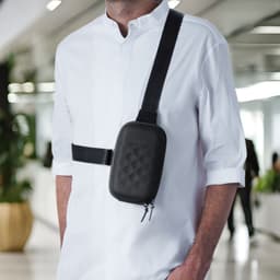 A black roll-top mini bag worn across the body over a white shirt, featuring a quilted pattern and an adjustable strap.