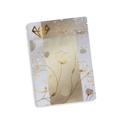 A small, metallic stand-up pouch in silver and gold, featuring floral designs and a logo.