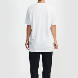 A white t-shirt with short sleeves is displayed on a person from the back, paired with black trousers. The shirt features a logo.