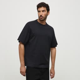 A black essential tee displayed on a model, featuring a relaxed fit and short sleeves. It has a logo on the garment.