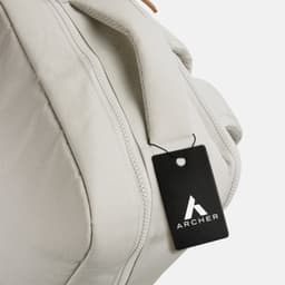 A light grey backpack with a handle and a tag attached, featuring a logo.
