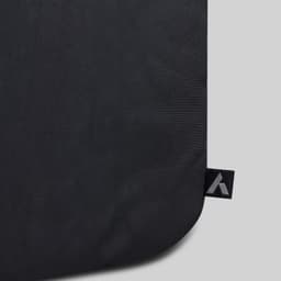 A close-up of a black fabric travel backpack featuring a logo tag on the edge.