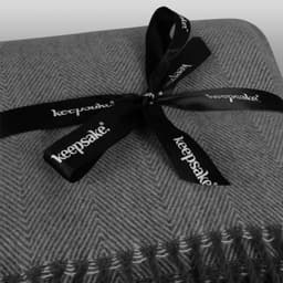 A grey patterned throw blanket tied with a black ribbon featuring a logo.